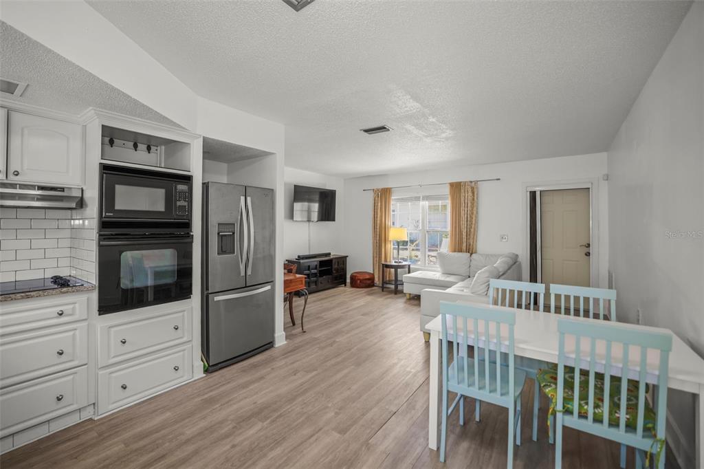 A kitchen and living area featuring white cabinets, stainless steel appliances, and light wood flooring — 7743 39TH TERRACE N, ST PETERSBURG, FL