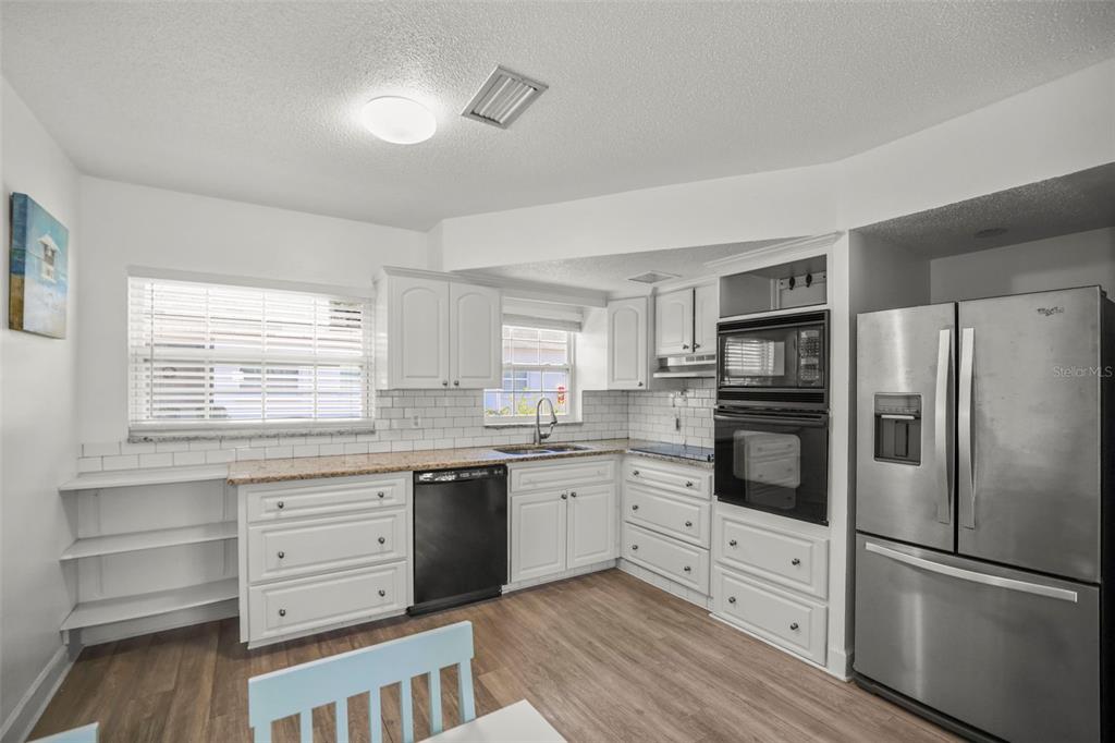 A kitchen with white cabinets, stainless steel appliances, granite countertops, and light wood flooring — 7743 39TH TERRACE N, ST PETERSBURG, FL