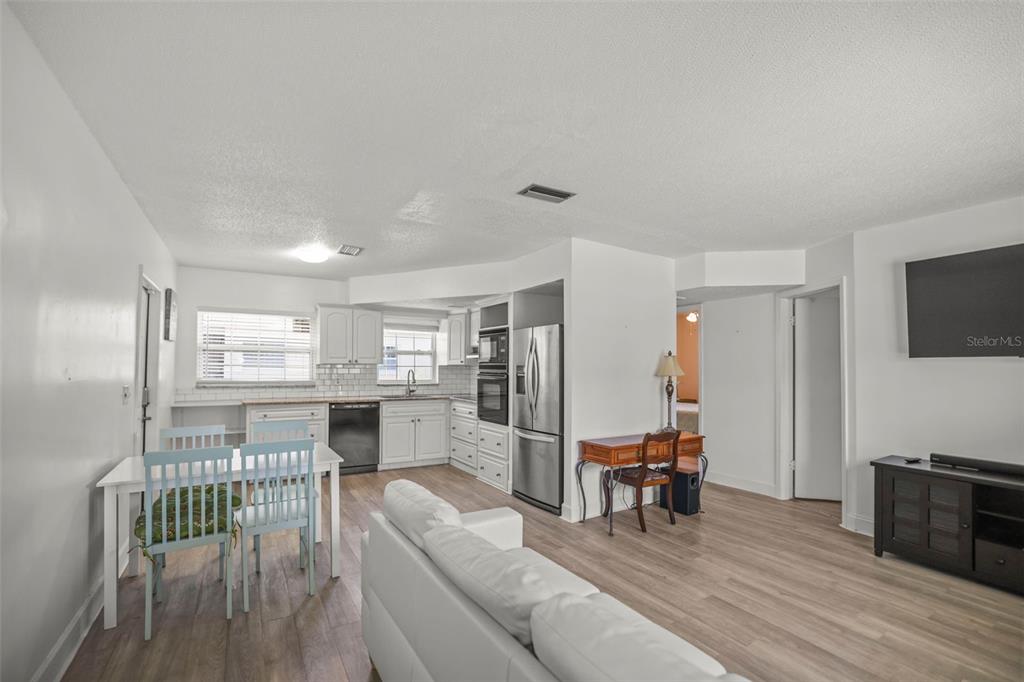 An open-concept living and dining area features white cabinets, stainless appliances, and light wood flooring — 7743 39TH TERRACE N, ST PETERSBURG, FL
