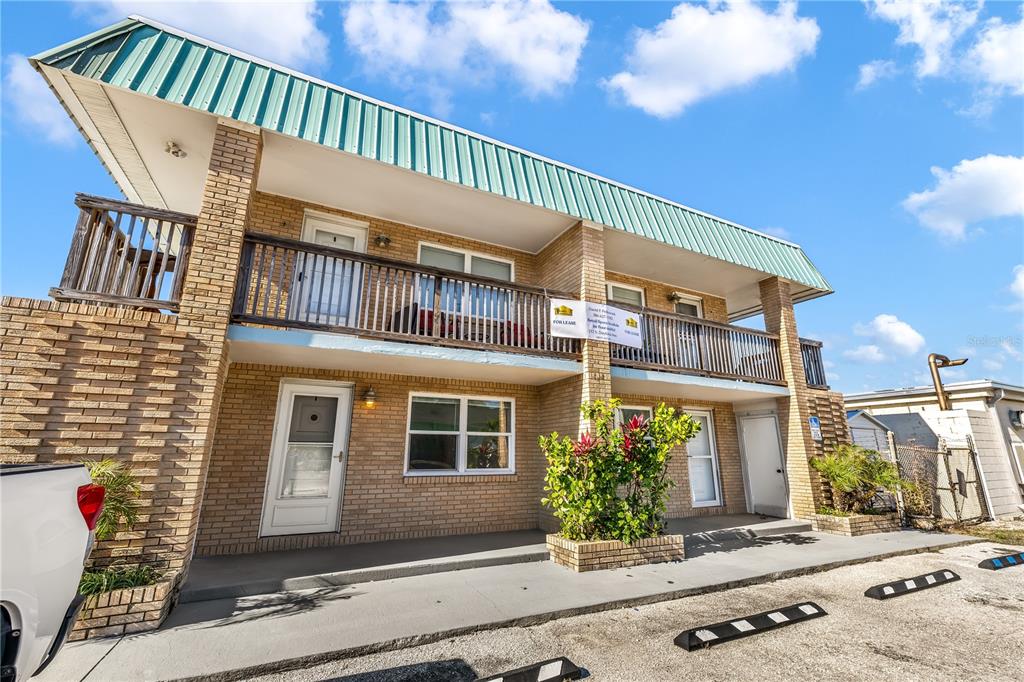 A two-story brick commercial building features a green metal roof and a second-floor balcony — 212 S DAYTONA AVENUE UNIT 1, FLAGLER BEACH, FL