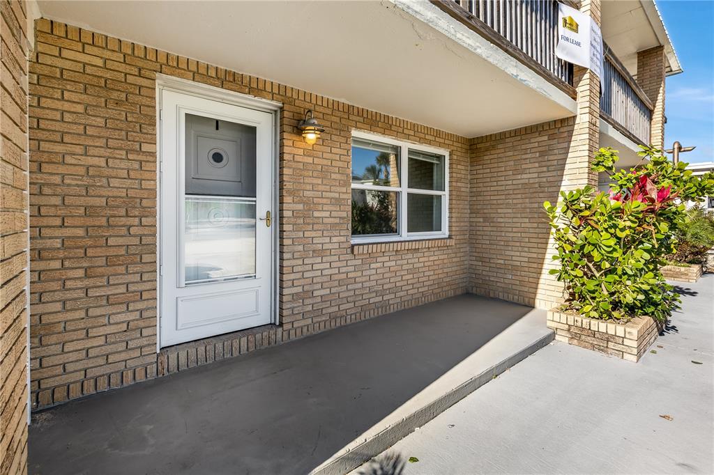 A brick exterior building features a white storm door, a window, and a small porch — 212 S DAYTONA AVENUE UNIT 1, FLAGLER BEACH, FL
