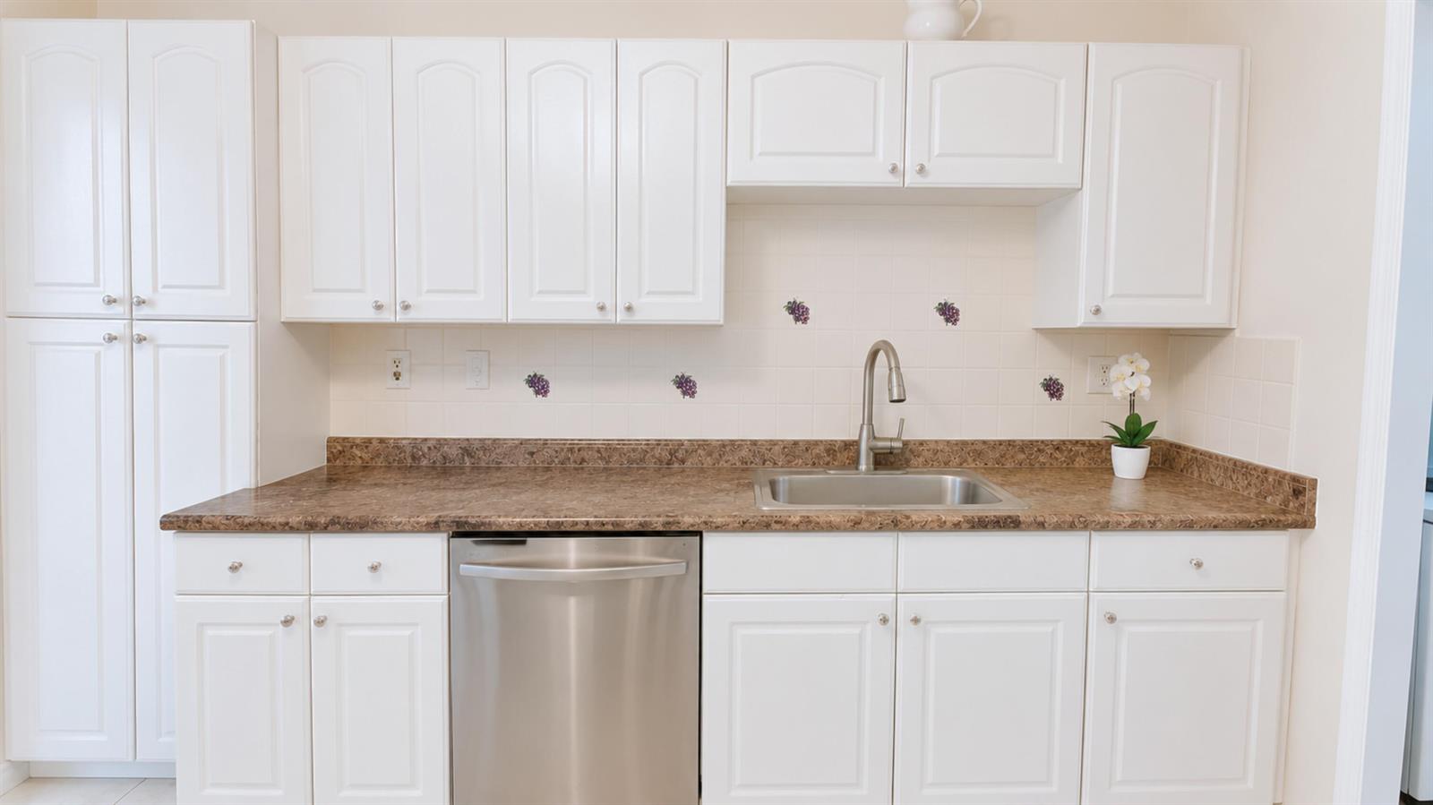 A kitchen features white cabinets, brown laminate countertops, a stainless steel dishwasher, and a sink — 3450 Blue Lake Drive # 204, Pompano Beach FL 33064, POMPANO BEACH, FL
