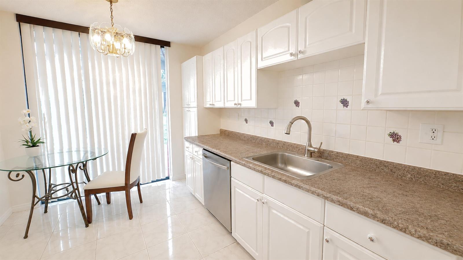 A kitchen features white cabinets, a stainless steel sink, and a dining area with glass table — 3450 Blue Lake Drive # 204, Pompano Beach FL 33064, POMPANO BEACH, FL
