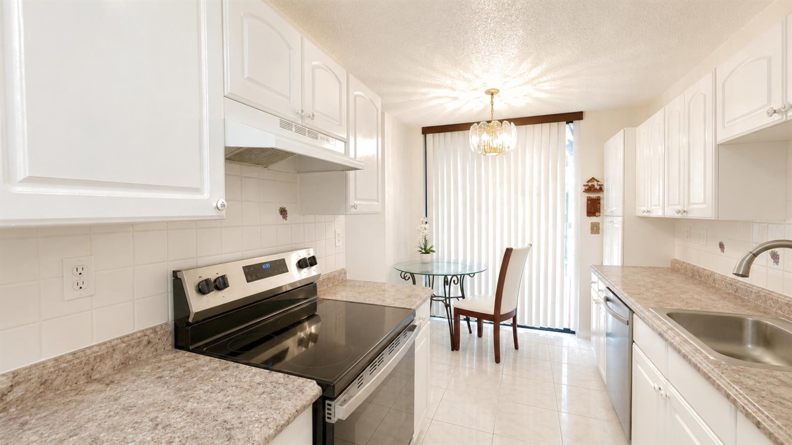 A kitchen features white cabinets, laminate countertops, a black stove, and a dining area — 3450 Blue Lake Drive # 204, Pompano Beach FL 33064, POMPANO BEACH, FL