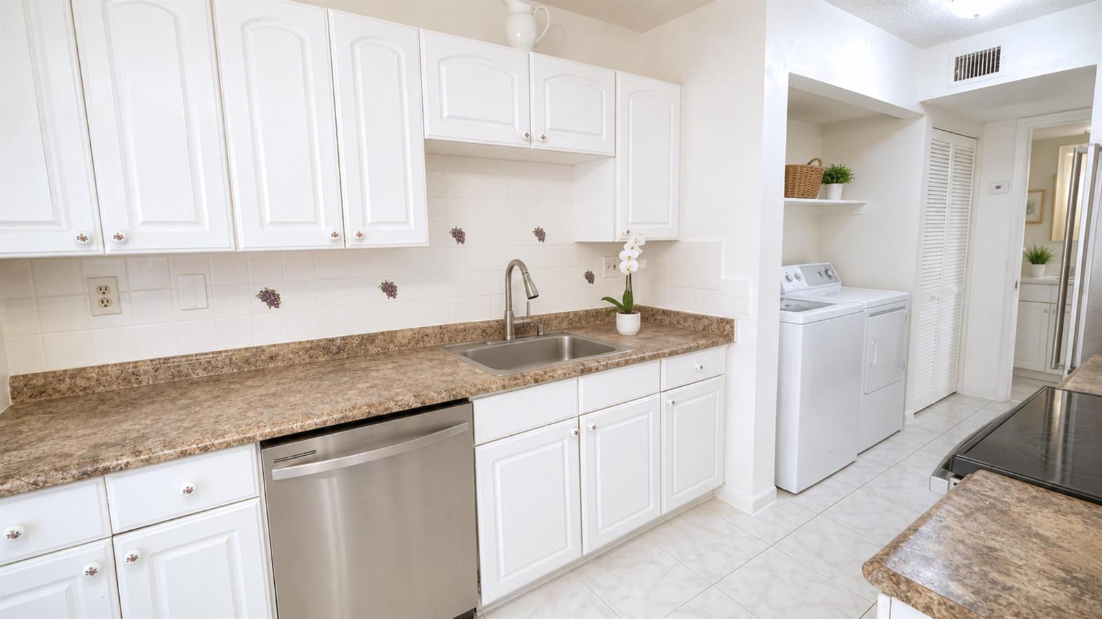 A kitchen with white cabinets, brown countertops, a stainless steel dishwasher, and an adjacent laundry area — 3450 Blue Lake Drive # 204, Pompano Beach FL 33064, POMPANO BEACH, FL