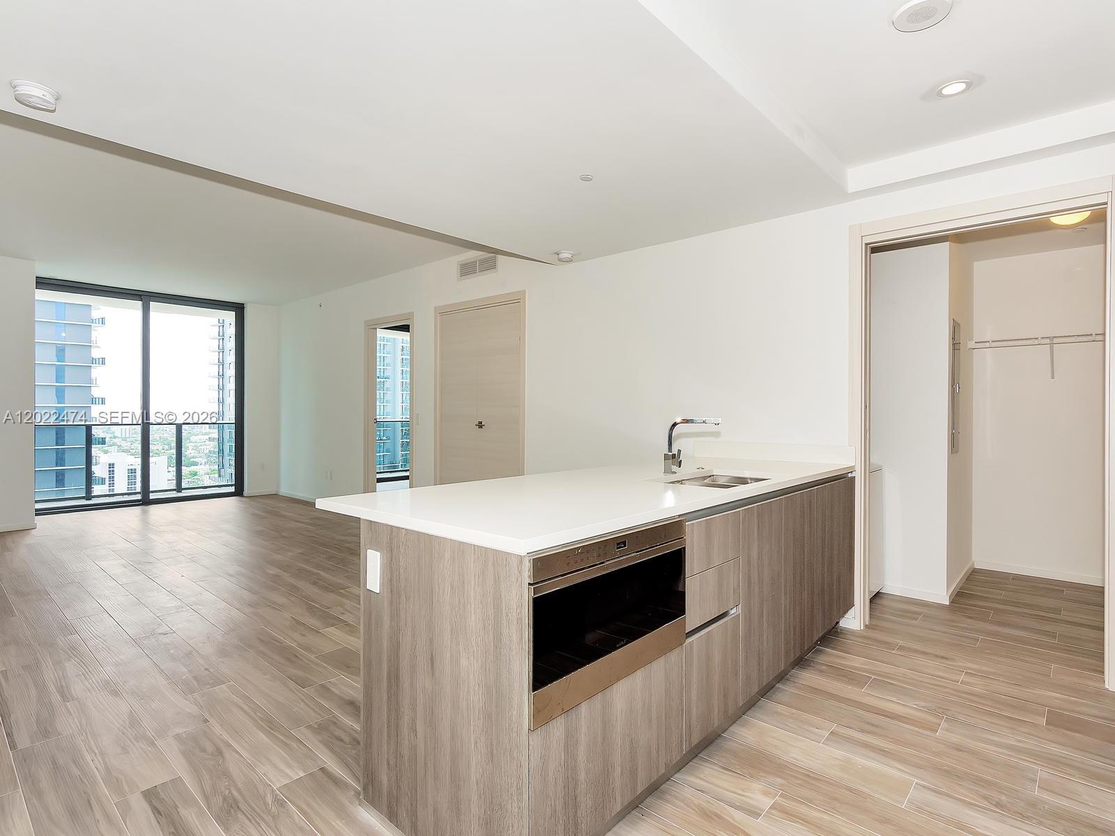 A modern kitchen island with a built-in oven sits in an open-plan apartment with wood-look flooring — 801 S Miami Ave # 2310, Miami FL 33131, MIAMI, FL