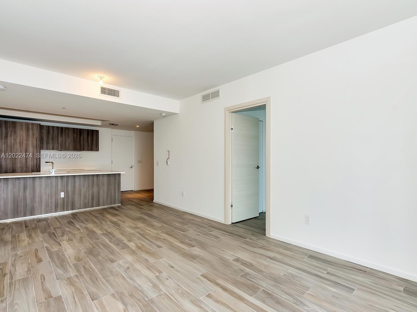 An open-concept living area features wood-look tile flooring, a kitchen island, and white walls — 801 S Miami Ave # 2310, Miami FL 33131, MIAMI, FL