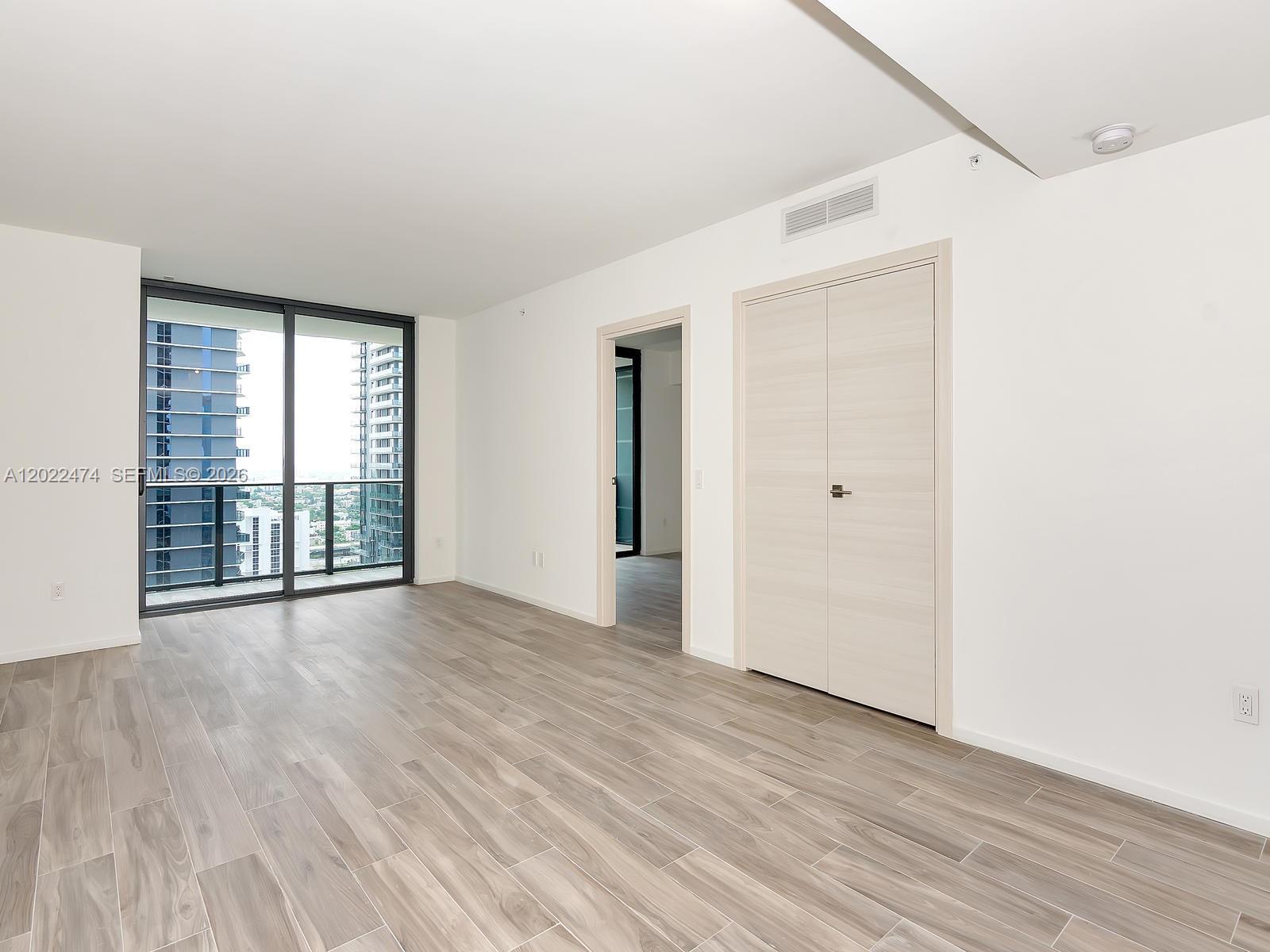 An empty room features light wood-look tile flooring, white walls, and a balcony with city views — 801 S Miami Ave # 2310, Miami FL 33131, MIAMI, FL
