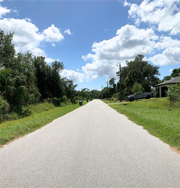 A paved road stretches into the distance, flanked by grassy verges, trees, and a parked truck — 2120 LORRAINE DRIVE, PORT CHARLOTTE, FL