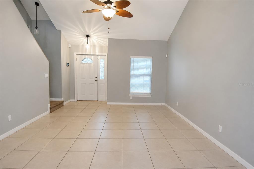An empty living room features light gray walls, beige tile flooring, and a vaulted ceiling — 183 HIGHLAND ROAD, TARPON SPRINGS, FL