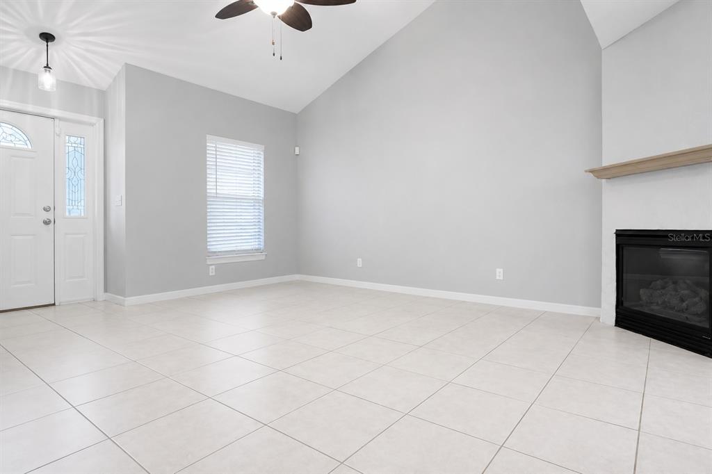 A living room with white tile floors, a vaulted ceiling, and a fireplace — 183 HIGHLAND ROAD, TARPON SPRINGS, FL