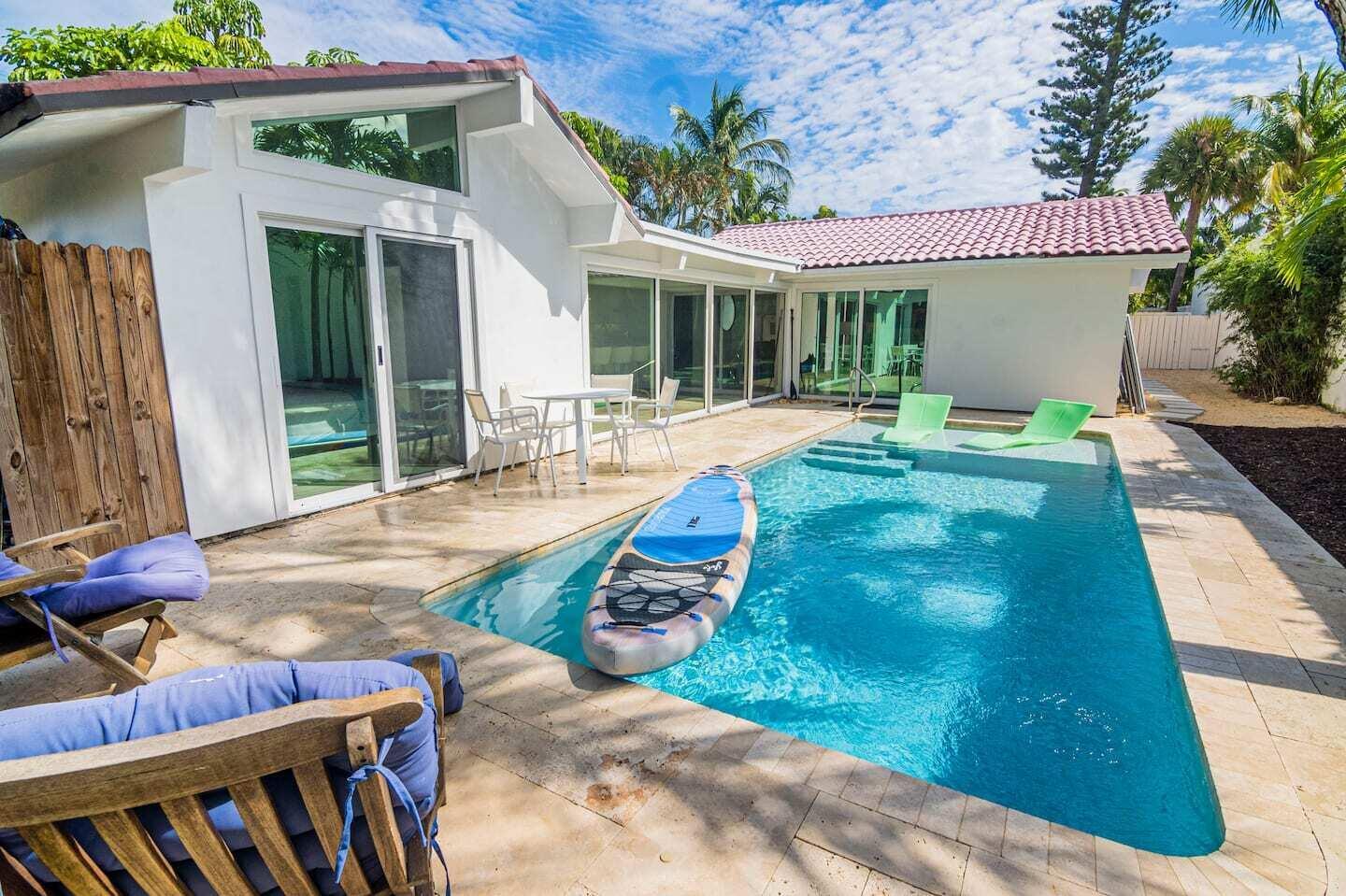 A backyard swimming pool with a paddleboard sits beside a white house with sliding doors — 103 W Sandpiper Circle W, Jupiter FL 33477, JUPITER, FL