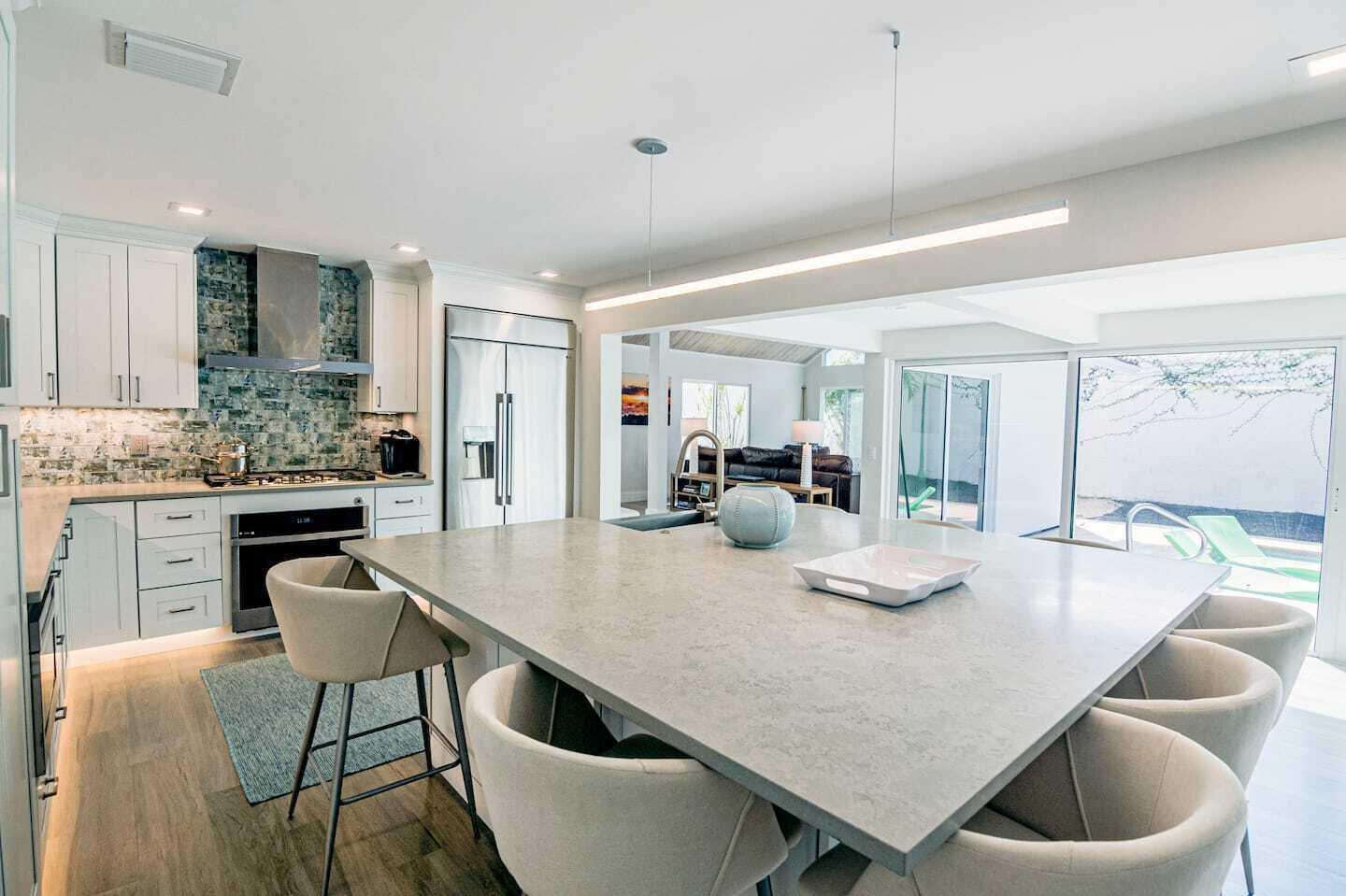 A modern kitchen features a large gray island, white cabinetry, and a blue tiled backsplash — 103 W Sandpiper Circle W, Jupiter FL 33477, JUPITER, FL