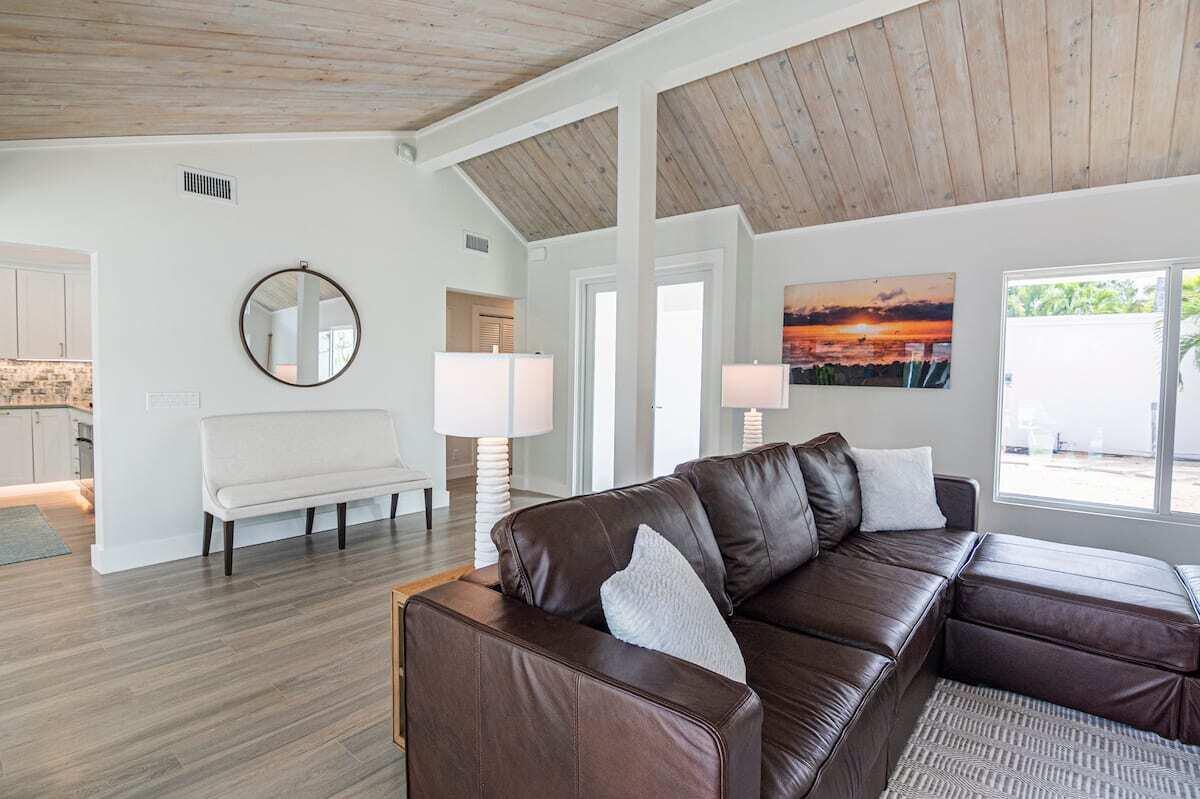 A living room features a brown leather sectional, wood-paneled vaulted ceilings, and a white bench — 103 W Sandpiper Circle W, Jupiter FL 33477, JUPITER, FL