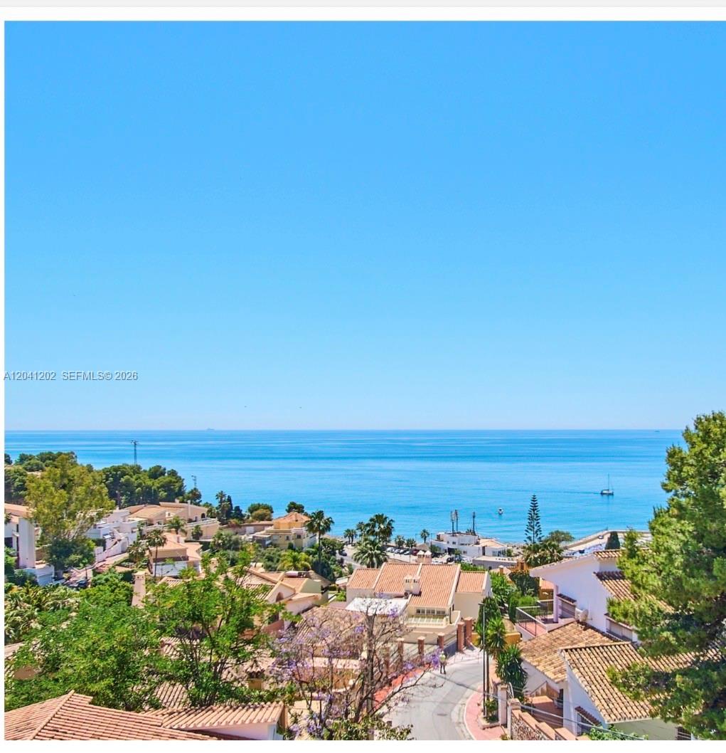 A high-angle view of a coastal neighborhood with terracotta-roofed houses overlooking the blue ocean — 29018 MALAGA, ESPAIN, FL
