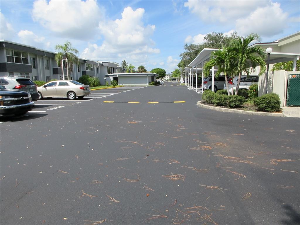 An outdoor parking lot with covered spaces, palm trees, and apartment buildings under a blue sky — 21320 BRINSON AVENUE UNIT 119, PORT CHARLOTTE, FL