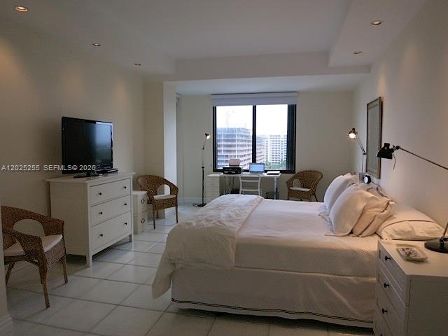 A bedroom with a white bed, dresser, desk, and wicker chairs on a tiled floor — 201 Crandon Blvd # 1027, Key Biscayne FL 33149, KEY BISCAYNE, FL