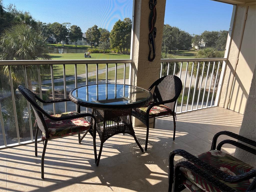 A screened-in balcony features a glass-topped wicker table and chairs overlooking a golf course — 6501 STONE RIVER RD UNIT 306, BRADENTON, FL