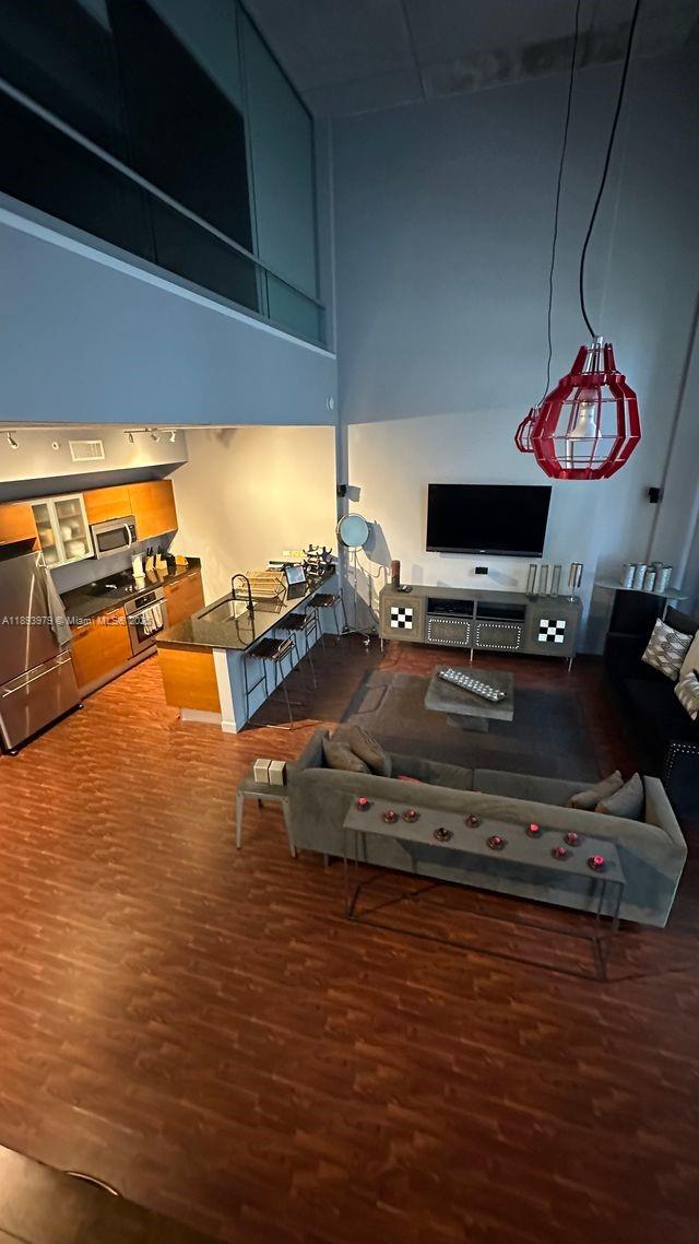 A high-ceilinged open-concept living room and kitchen with wood flooring and a red pendant light — 3449 NE 1st Ave # L43, Miami FL 33137, MIAMI, FL