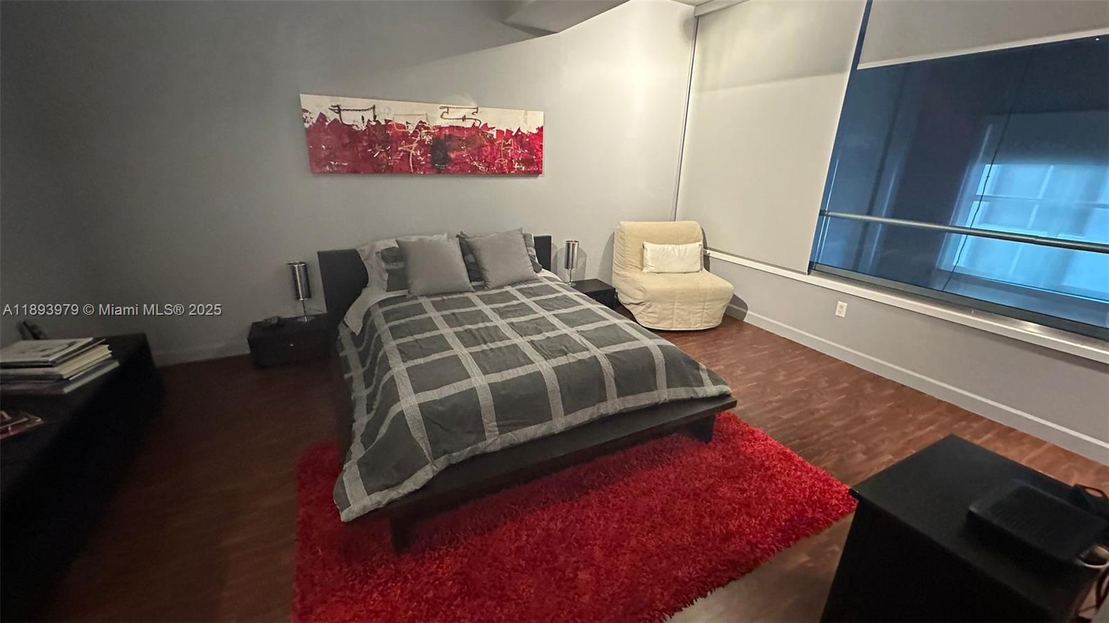 A bedroom features a bed with a plaid comforter, a red rug, and large windows — 3449 NE 1st Ave # L43, Miami FL 33137, MIAMI, FL