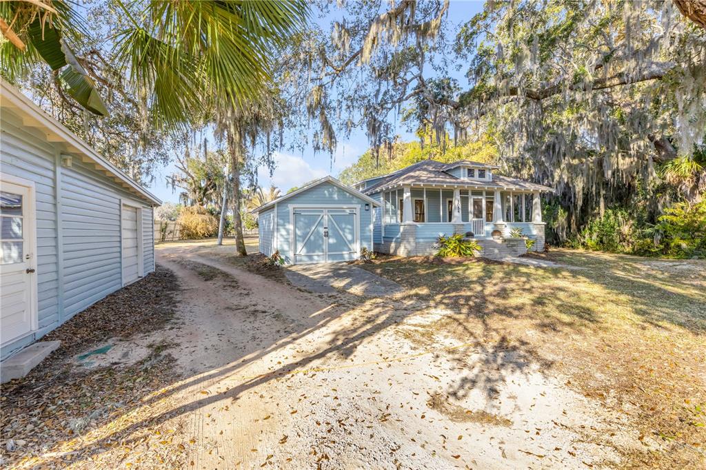 A light blue house with a detached garage sits on a sandy lot under trees — 3054 N DIXIE FREEWAY, NEW SMYRNA BEACH, FL
