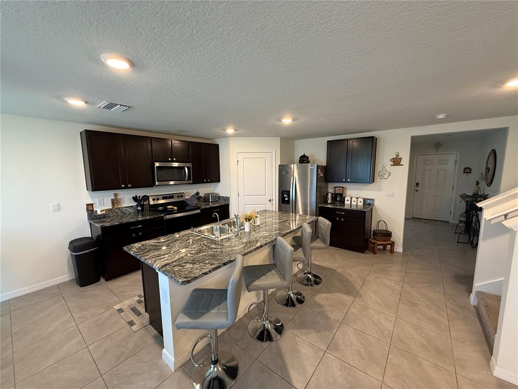 A kitchen features dark wood cabinets, granite countertops, a central island, and gray tile flooring — 4120 SILVER STRAND TRAIL, PALMETTO, FL