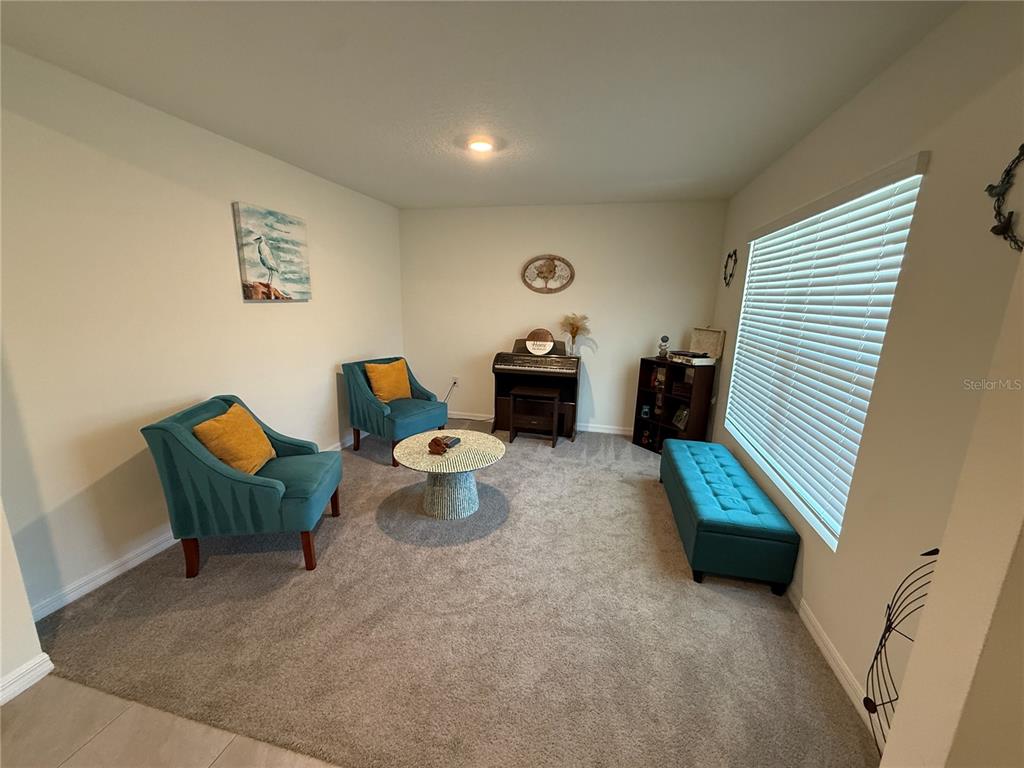 A carpeted living room features two teal armchairs, a matching bench, and a small piano — 4120 SILVER STRAND TRAIL, PALMETTO, FL