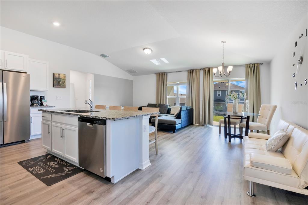 An open-concept kitchen and living area features light wood flooring, white cabinetry, and granite countertops — 9231 WESTSIDE HILLS DRIVE, DAVENPORT, FL