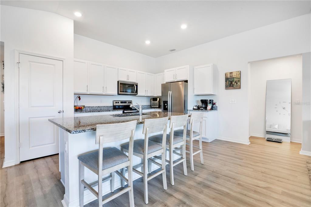 A kitchen features white cabinetry, granite countertops, a center island with four chairs, and flooring — 9231 WESTSIDE HILLS DRIVE, DAVENPORT, FL
