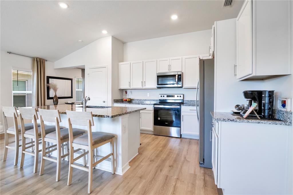 A kitchen features white cabinets, granite countertops, stainless steel appliances, and a breakfast bar island — 9231 WESTSIDE HILLS DRIVE, DAVENPORT, FL