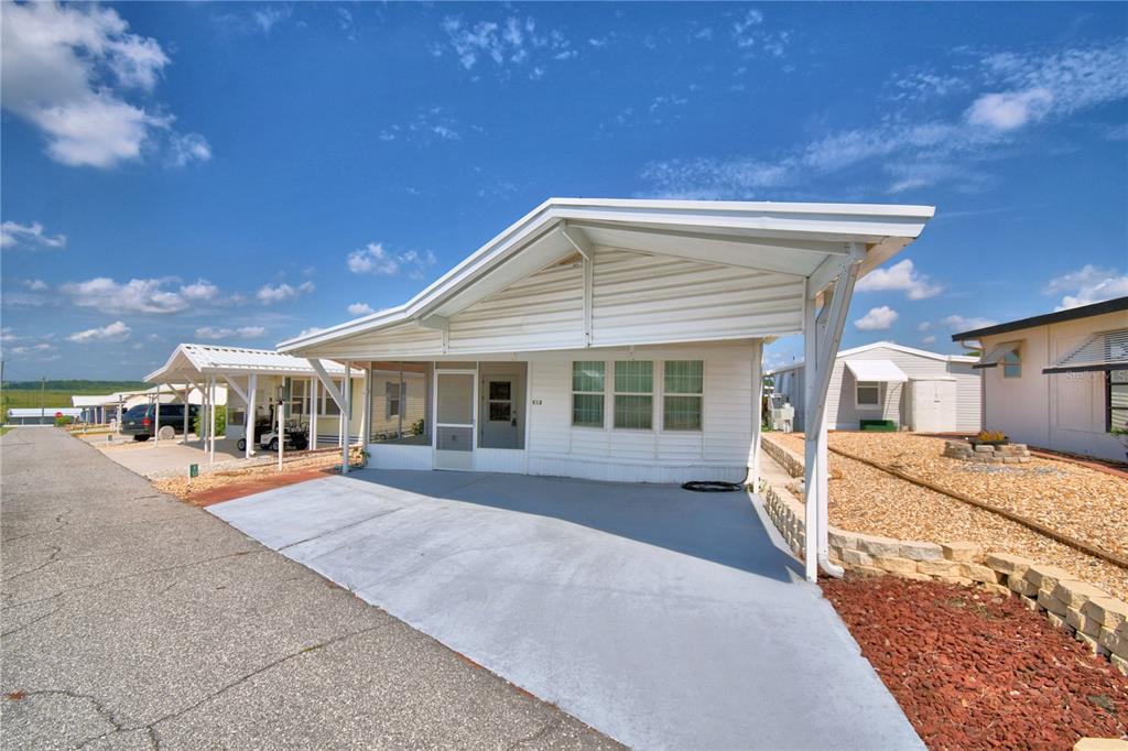 A white manufactured home with a carport and a screened-in front porch under a blue sky — 251 PATTERSON ROAD UNIT E12, HAINES CITY, FL