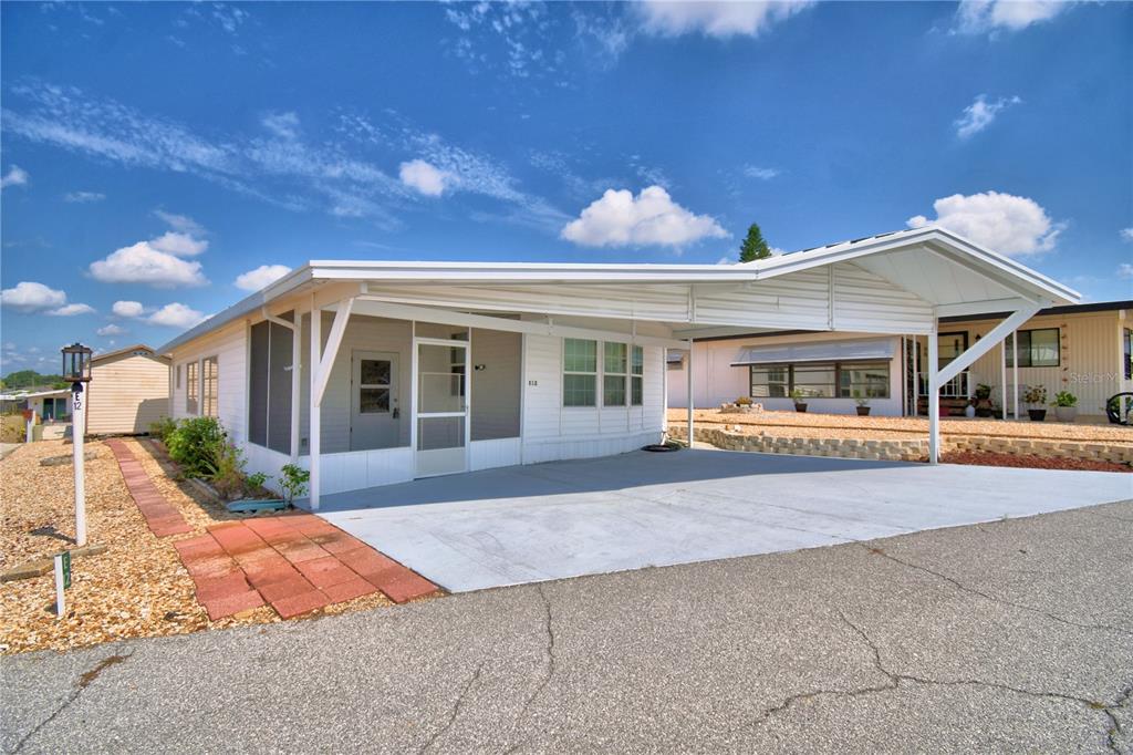 A white manufactured home features a large attached carport and a screened-in front porch — 251 PATTERSON ROAD UNIT E12, HAINES CITY, FL