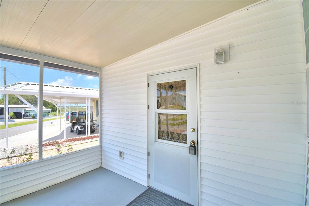 A covered porch features white vinyl siding, a glass-paneled door, and a view of a carport — 251 PATTERSON ROAD UNIT E12, HAINES CITY, FL