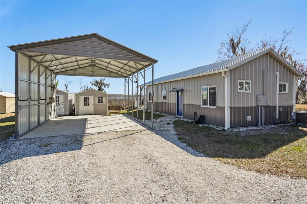A metal-sided house with a large attached carport and two small storage sheds nearby — 645 CR 485A, LAKE PANASOFFKEE, FL