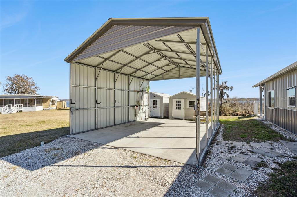 An open-sided metal carport with a concrete floor sits between two small storage sheds — 645 CR 485A, LAKE PANASOFFKEE, FL