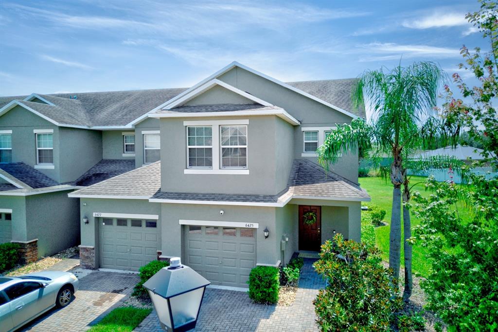 A two-story townhouse with a gray stucco exterior, two garage doors, and a palm tree — 6425 TORRINGTON CIRCLE, LAKELAND, FL