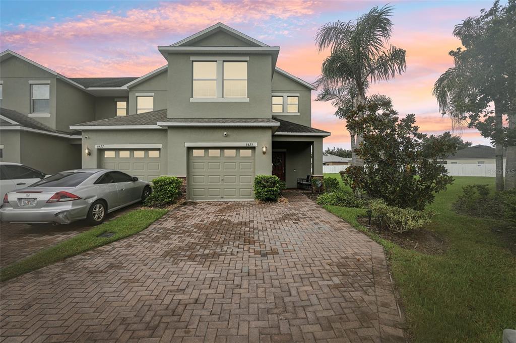 A two-story townhouse with a paver driveway, a garage, and a palm tree at sunset — 6425 TORRINGTON CIRCLE, LAKELAND, FL