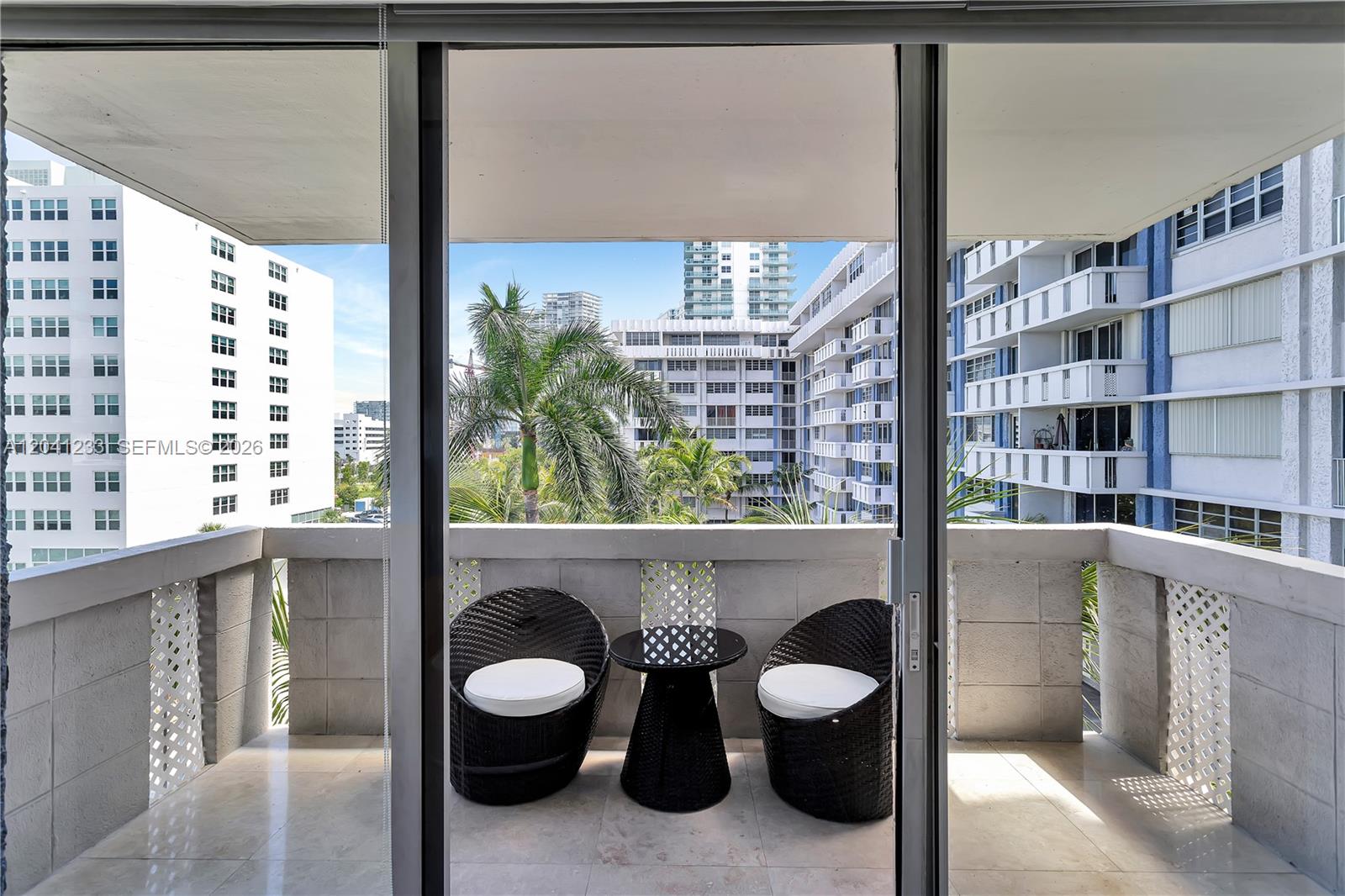 A balcony features two dark wicker chairs and a small table overlooking urban buildings — 800 West Ave # 635, Miami Beach FL 33139, MIAMI BEACH, FL