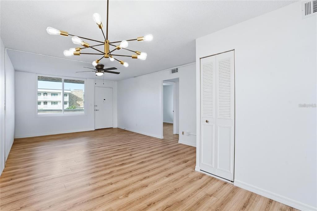 An empty living room features light wood-look flooring, white walls, and a modern sputnik chandelier — 5095 BAY STREET NE UNIT 21O, ST PETERSBURG, FL