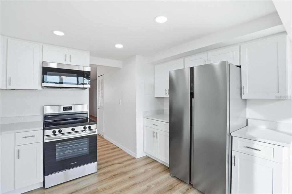 A kitchen with white cabinets, stainless steel appliances, and light wood-look flooring — 5095 BAY STREET NE UNIT 21O, ST PETERSBURG, FL