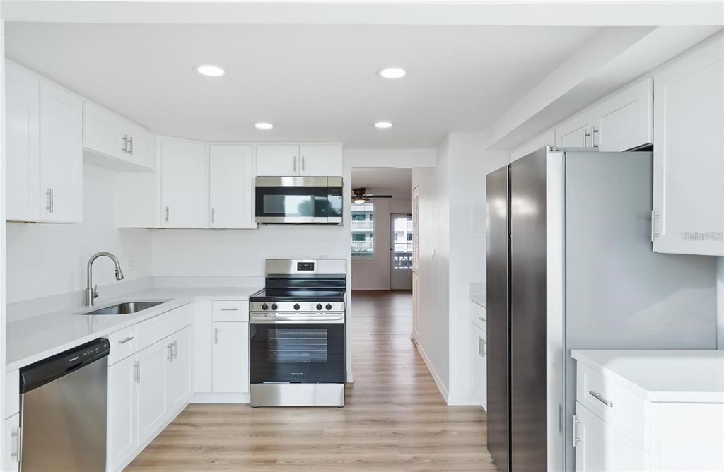 A modern kitchen features white cabinets, stainless steel appliances, and light wood-look flooring — 5095 BAY STREET NE UNIT 21O, ST PETERSBURG, FL