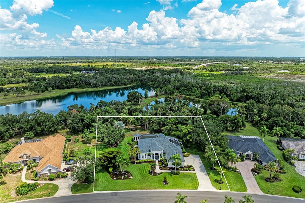 An aerial view shows a house with a pool cage surrounded by trees and water — 2362 LITTLE COUNTRY ROAD, PARRISH, FL
