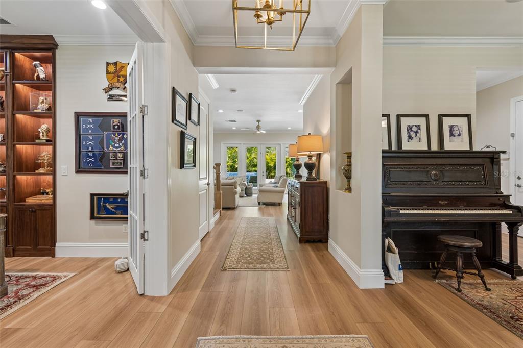 A hallway with light wood flooring leads past a piano and built-in shelving toward a living area — 4601 S ESPERANZA AVENUE, TAMPA, FL