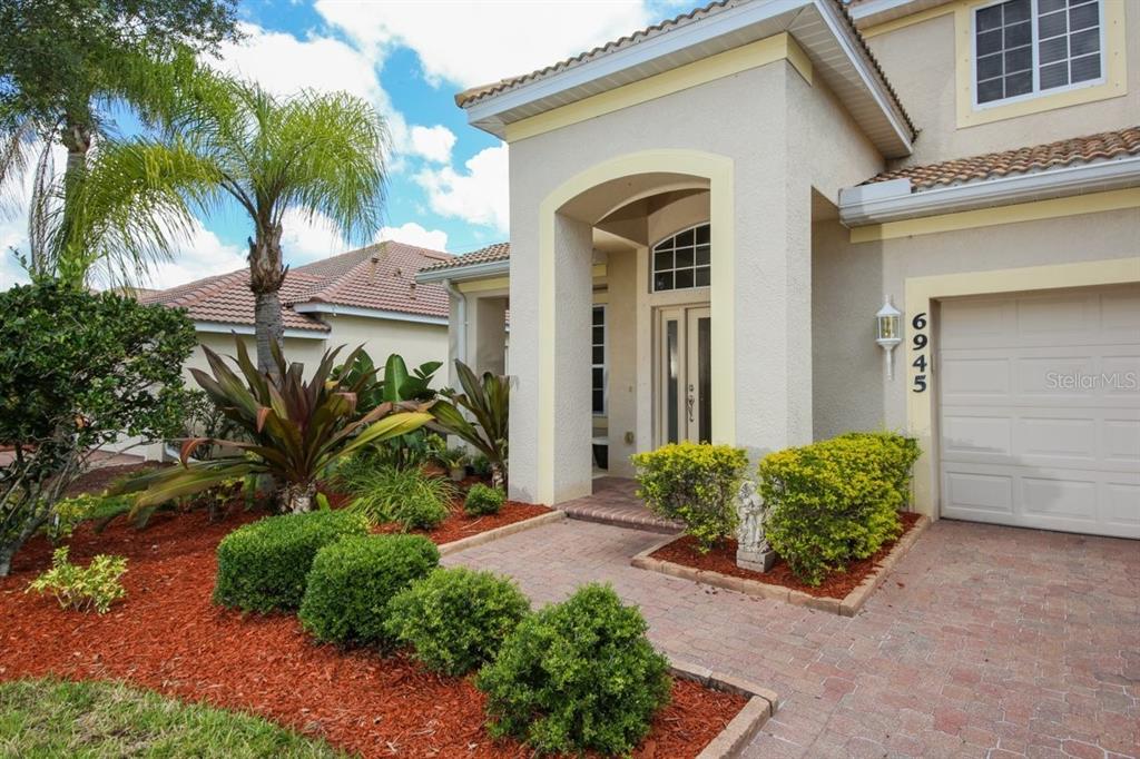 The exterior of a two-story stucco home features a brick walkway and a garage — 6945 74TH STREET CIRCLE E, BRADENTON, FL