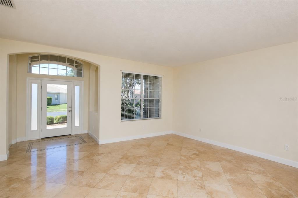 An empty room with beige walls, tile flooring, a front door, and a large window — 6945 74TH STREET CIRCLE E, BRADENTON, FL