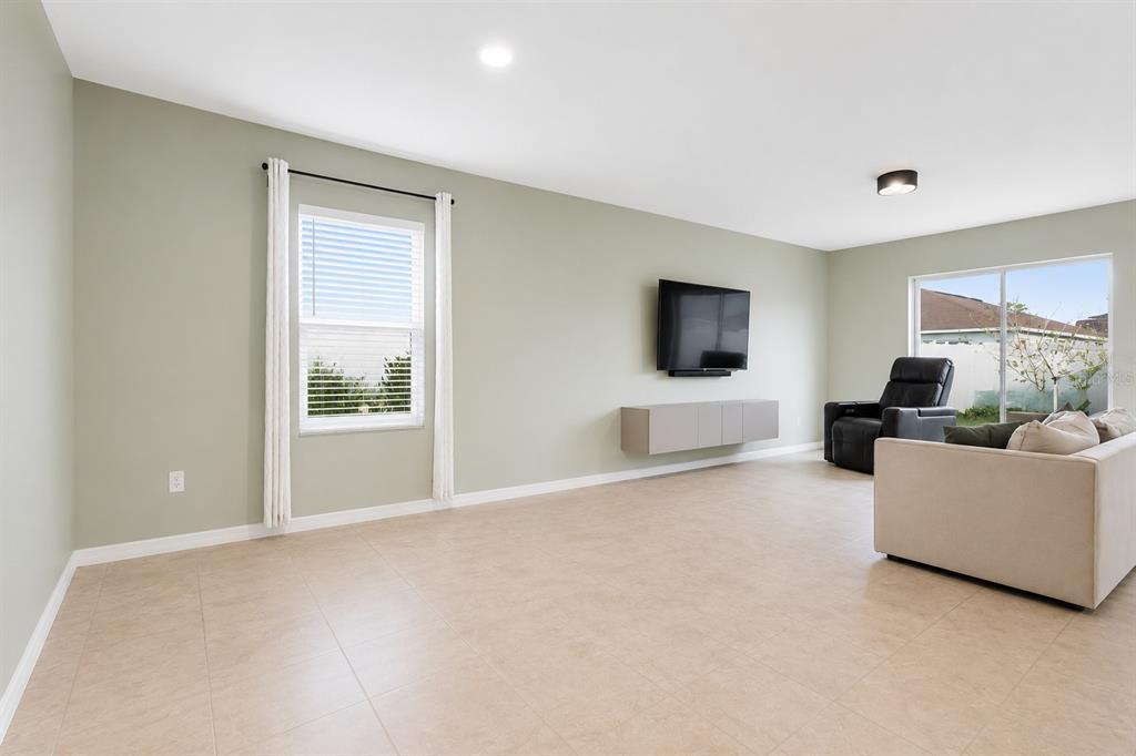 A living room with light green walls, tile flooring, a wall-mounted television, and sliding doors — 10624 MASSIMO DRIVE, WIMAUMA, FL
