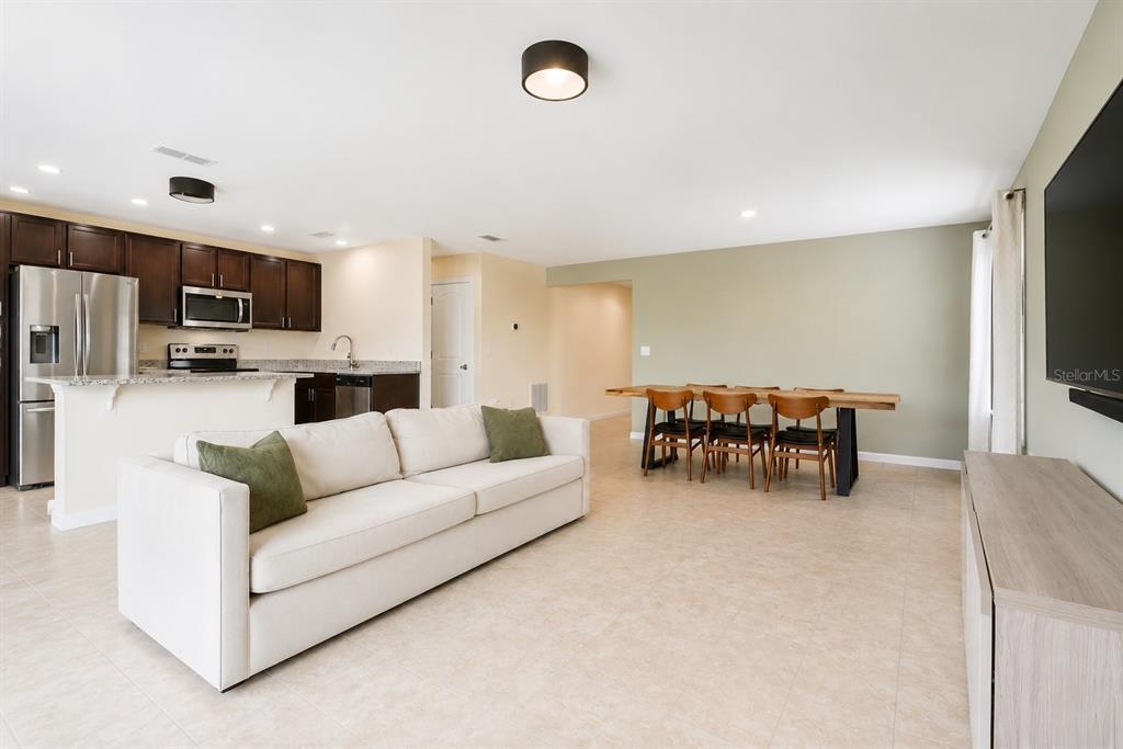 An open-concept living and dining area features a white sofa, wooden dining table, and kitchen — 10624 MASSIMO DRIVE, WIMAUMA, FL
