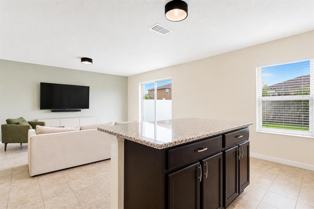 A kitchen island with dark cabinets and granite countertops overlooks a living room with tile floors — 10624 MASSIMO DRIVE, WIMAUMA, FL