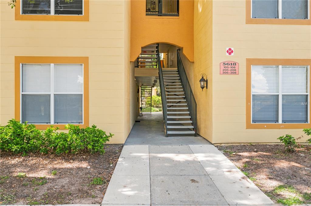 An exterior view of a multi-story apartment building featuring a central staircase and walkway — 5618 PINNACLE HEIGHTS CIRCLE UNIT 206, TAMPA, FL