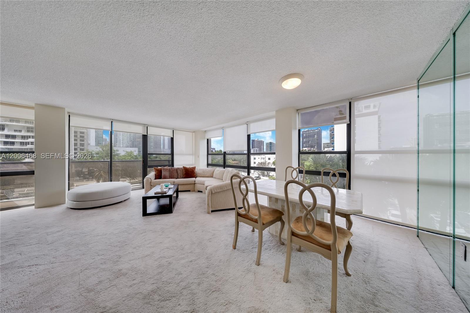 A living and dining area with wall-to-wall windows, carpeted floors, and city views — 600 NE 36th St # 421, Miami FL 33137, MIAMI, FL